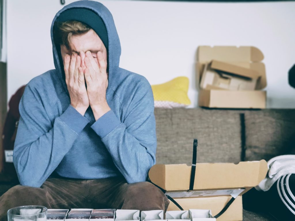A man wearing a blue hoodie holding his hands to his face