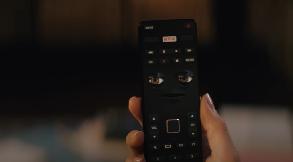A hand holding a remote with Netflix logo on a button and eyes