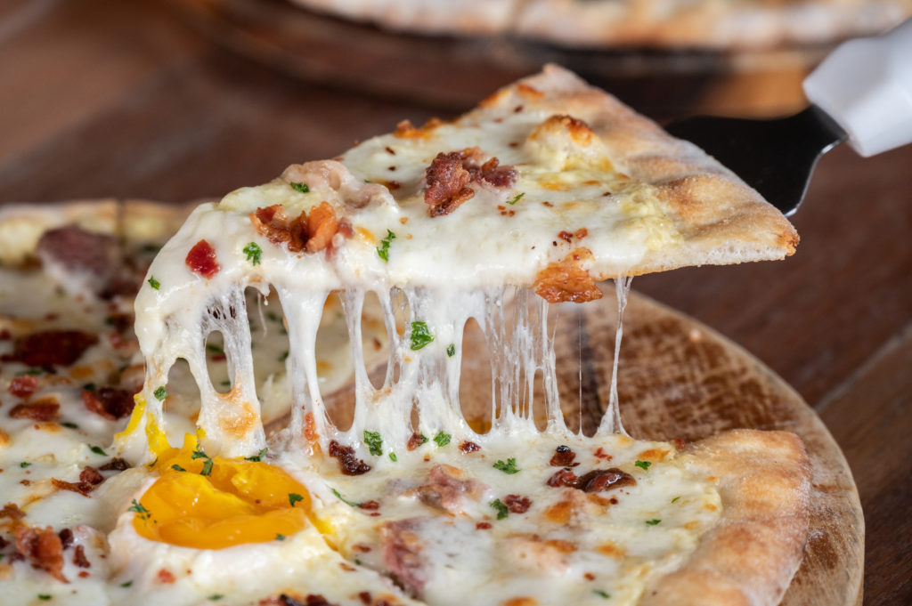 Someone using a peel for separate a piece of Carbonara pizza before eating.