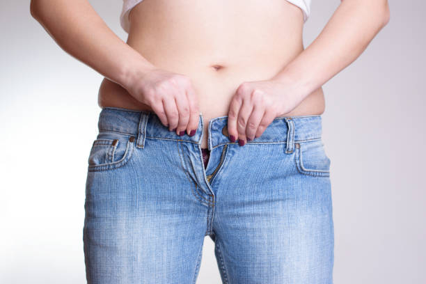 Young woman buttoning tight jeans - dieting concept