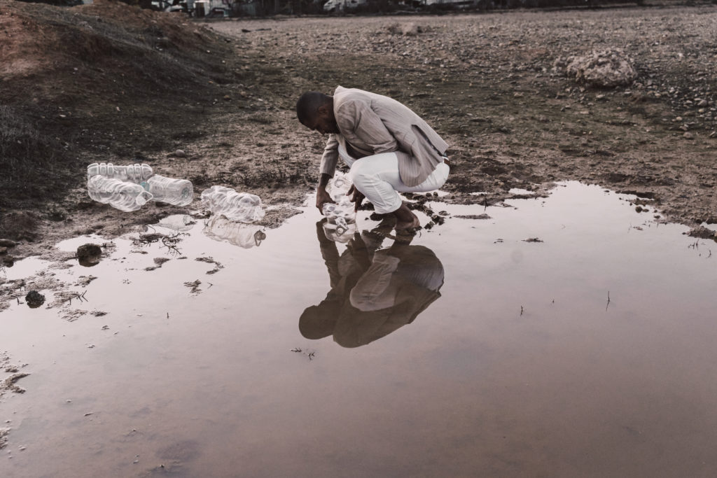 Young man filling plastic bottle with water at a water hole
